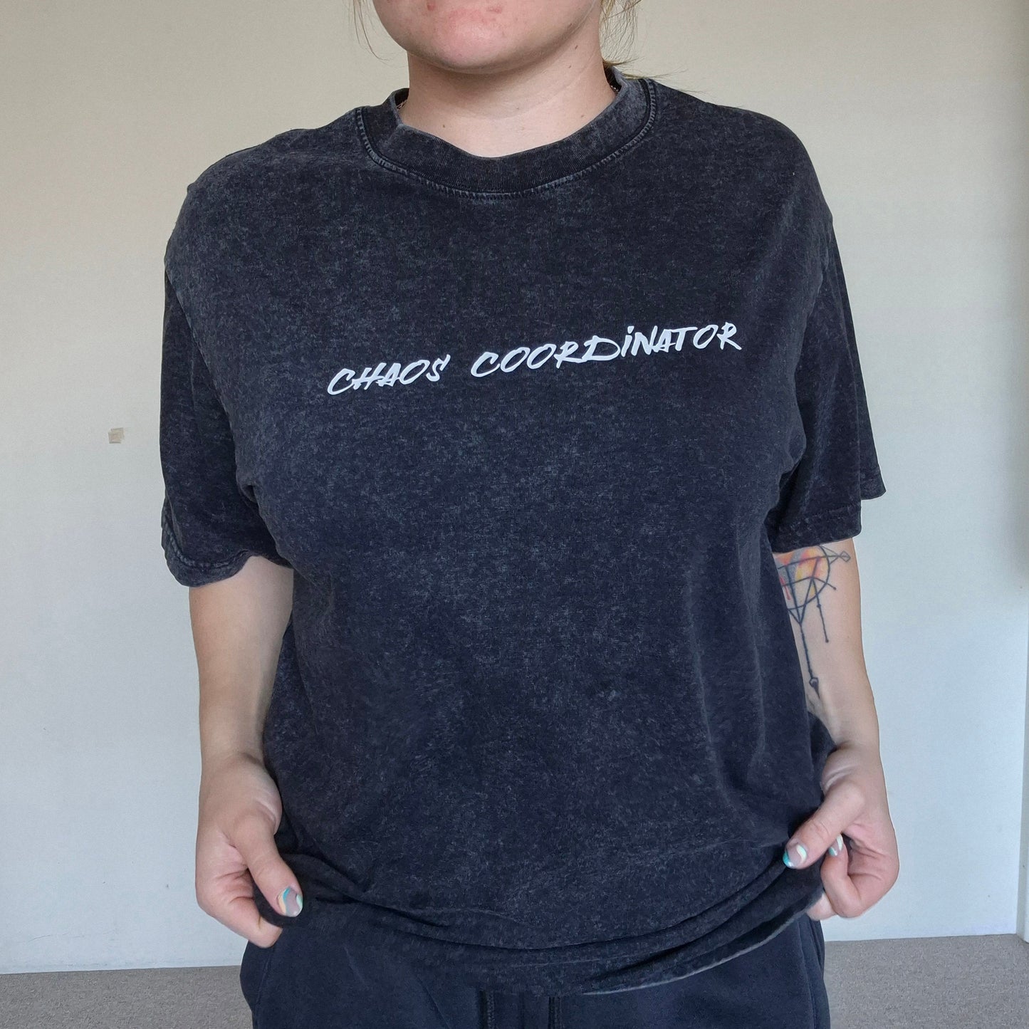 Person wearing a dark t-shirt with 'CHAOS COORDINATOR' text in a plain room.