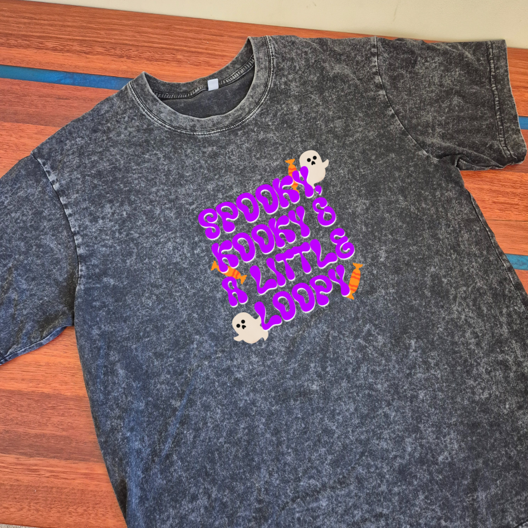 Black acid-wash t-shirt with colorful graphic design on a wooden surface